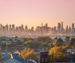 The Melbourne city skyline at dusk. There are inner-suburban houses and buildings in the foreground.