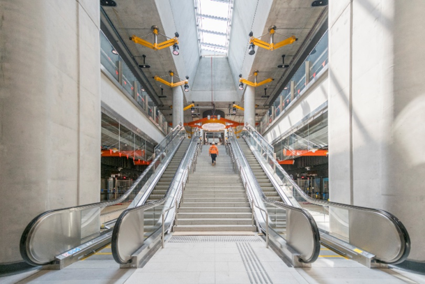 A photograph of Arden station showing 2 escalators and a flight of stairs with a worker walking up the stairs.