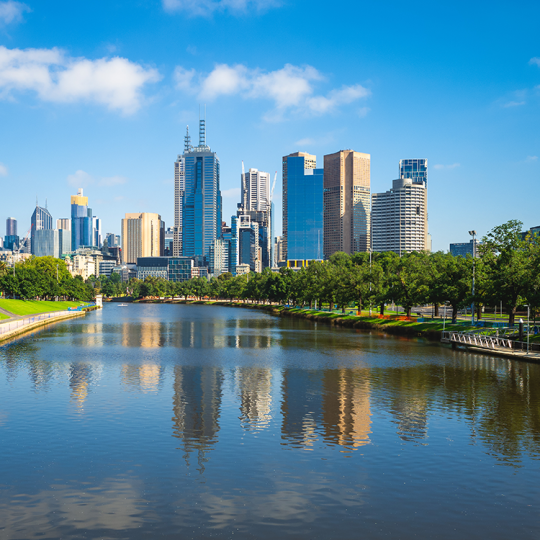 The Melbourne city skyline on a bright sunny day. The Yarra River is in the foreground and the buildings are reflected in the water.