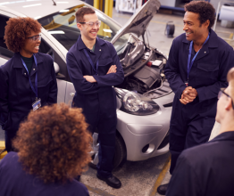 A group of TAFE mechanic students talking and laughing in a classroom workshop.