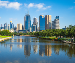 The Melbourne city skyline on a bright sunny day. The Yarra River is in the foreground and the buildings are reflected in the water.